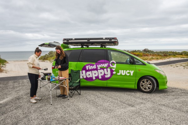 JUCY Crib Campervan Hire Parked on Beach with 2 friends using camping equipment