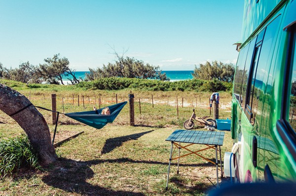 Beach front campsite with with parked campervan and kid playing in a swing hammock