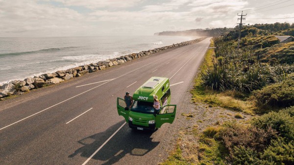 Condo campervan parked on ocean-side road with couple leaning out of each door