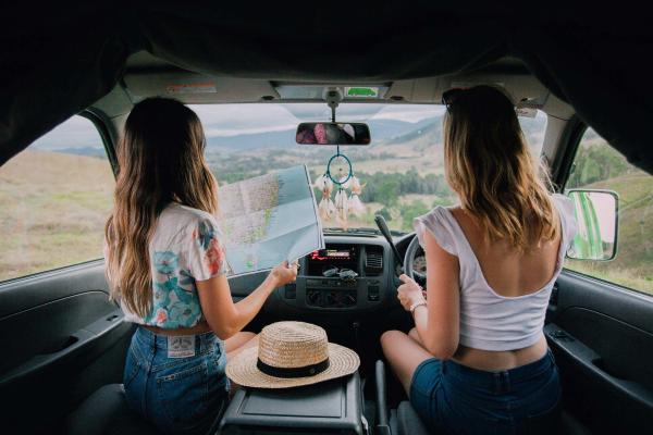 Two girls planning their route on a map behind the wheel of a JUCY campervan