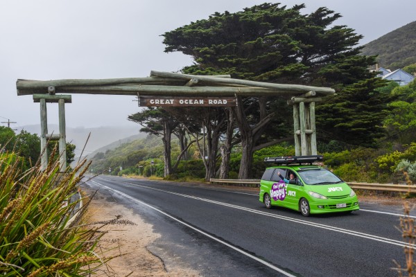 Lady driving and waving out of a Crib Plus campervan at the Great Ocean Road entrance sign