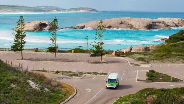 JUCY Coaster driving out of car park in Western Australia with ocean backdrop 