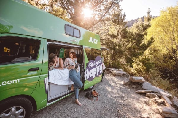 A couple leaning against a JUCY condo campervan enjoying a conversation