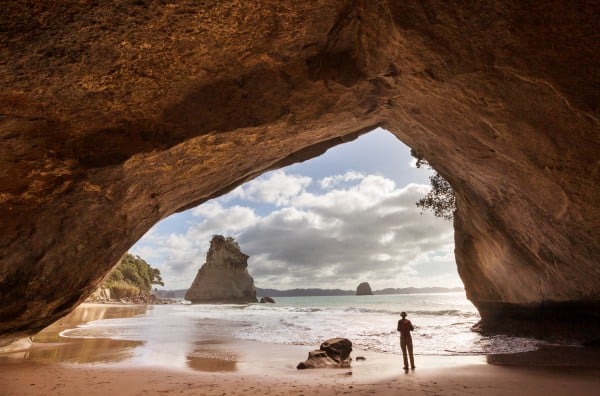 Lady standing under beach rock arch Coromandel Peninsula