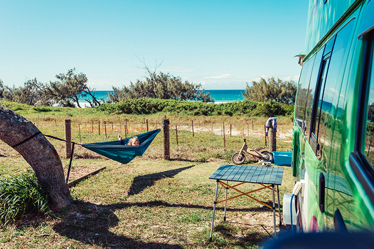 JUCY Condo parked on grass next to the beach with a kid in a hammock next to it