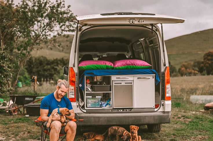 Man with a group of dogs sitting at the back of a campervan