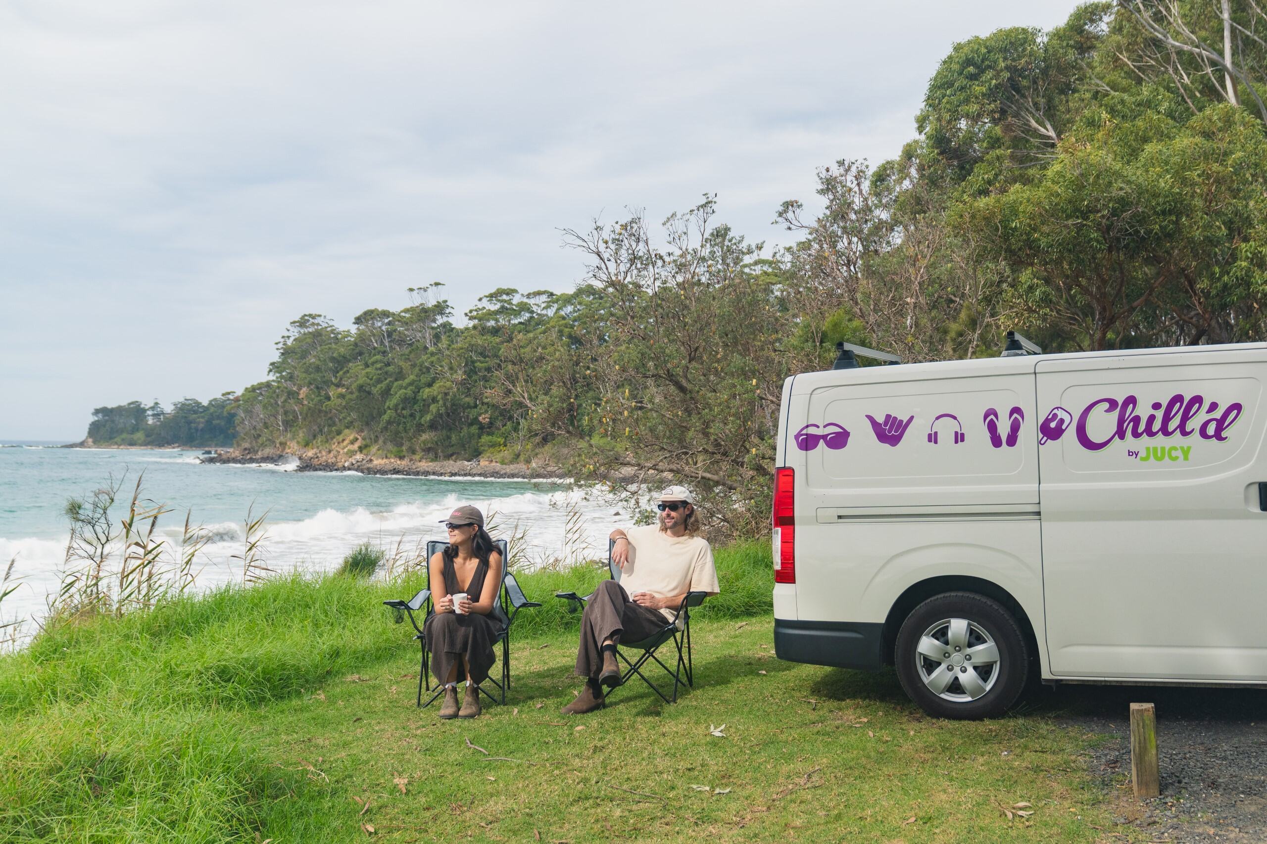Adam and Clara parked campervan on grassy hill overlooking ocean