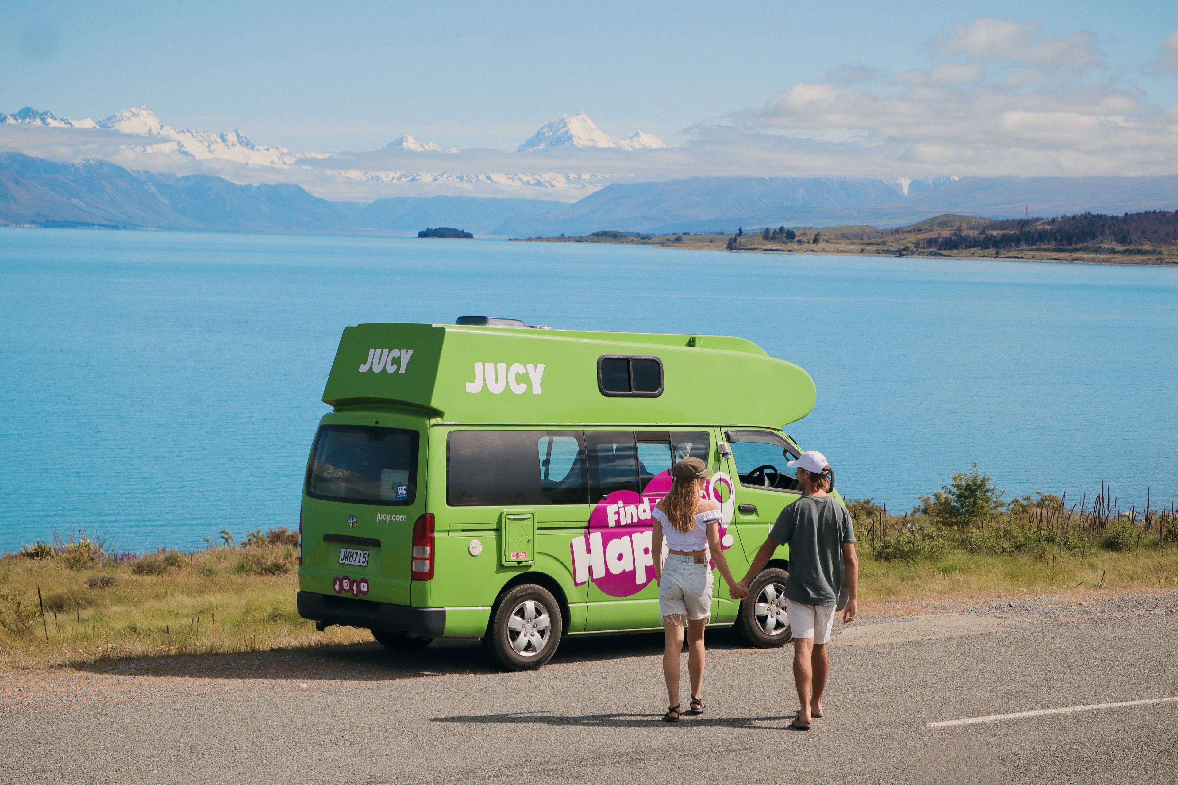 Couple walking toward JUCY condo campervan parked next to Lake Tekapo