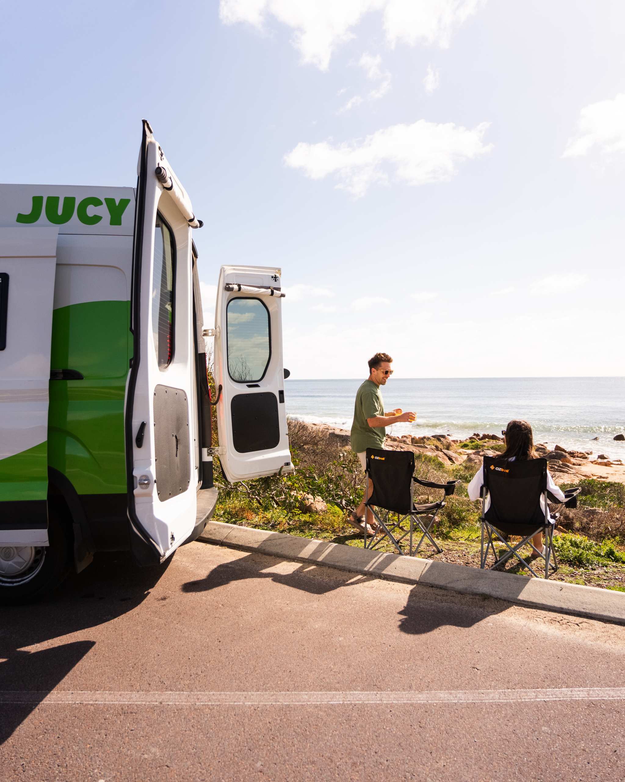 JUCY Coaster with couple sitting at the beach in camping chairs