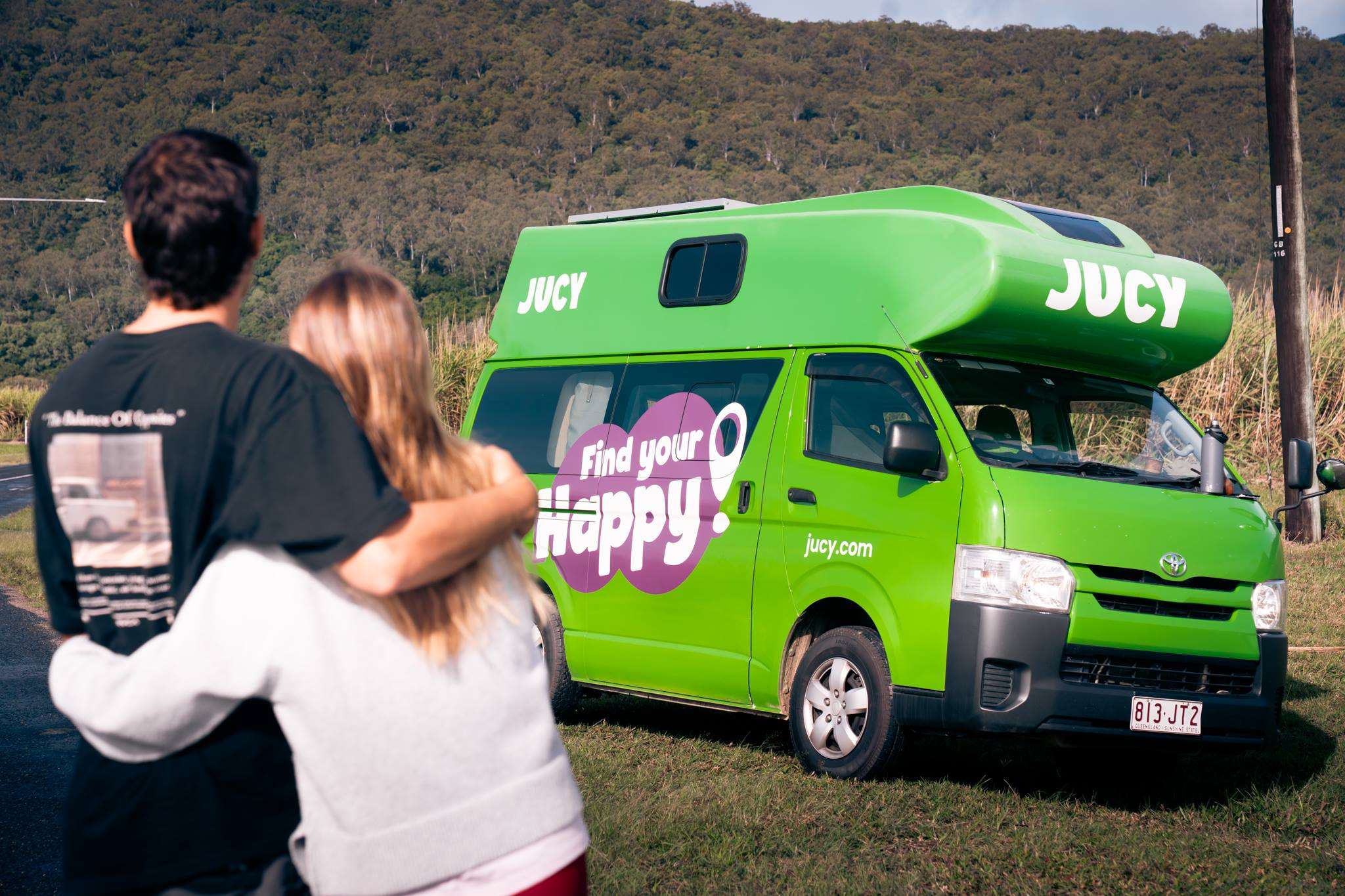 Couple hugging and looking at parked Condo campervan parked on grass
