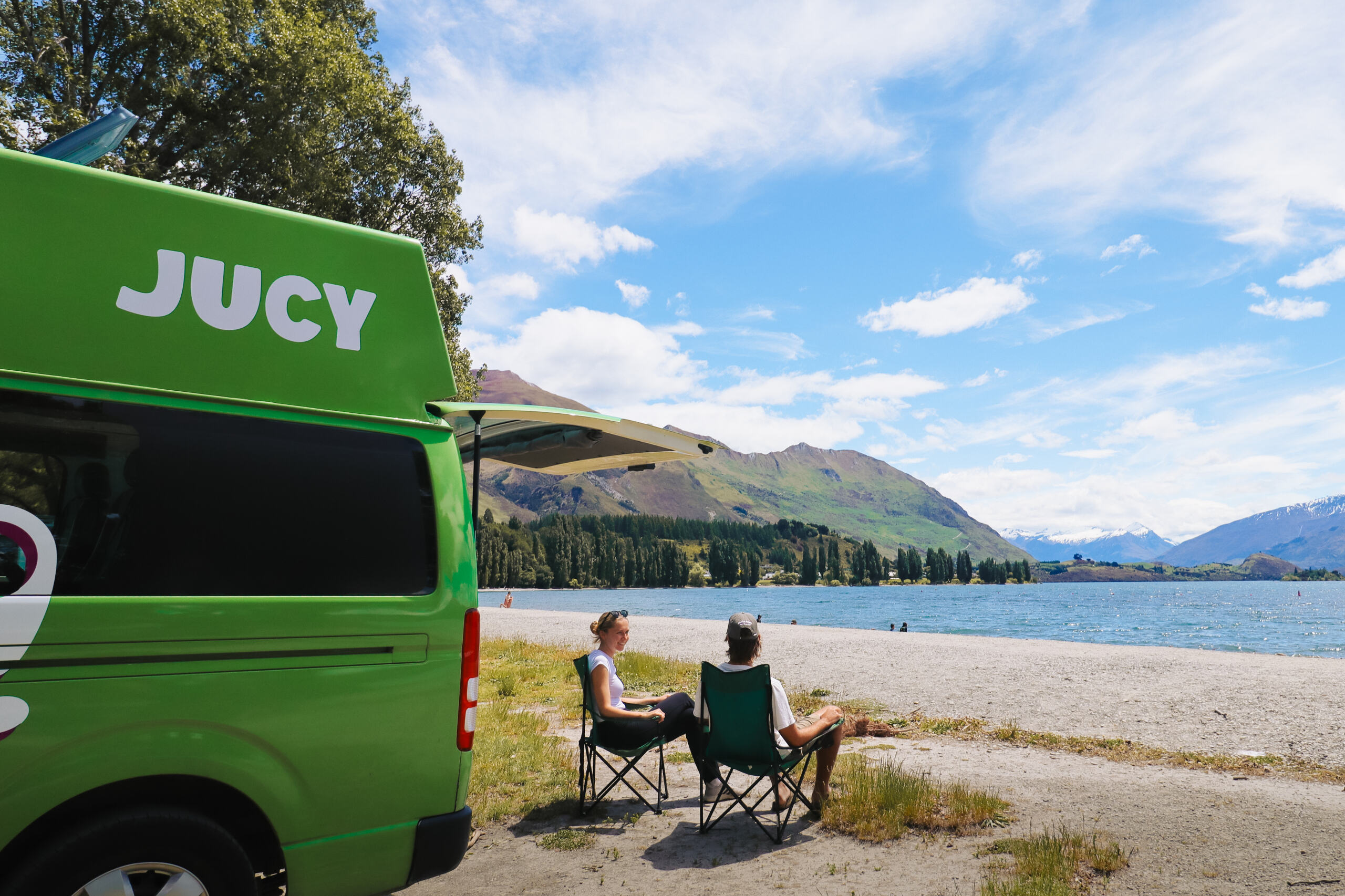 Couple Sitting beside a lake next to their JUCY Condo Campervan