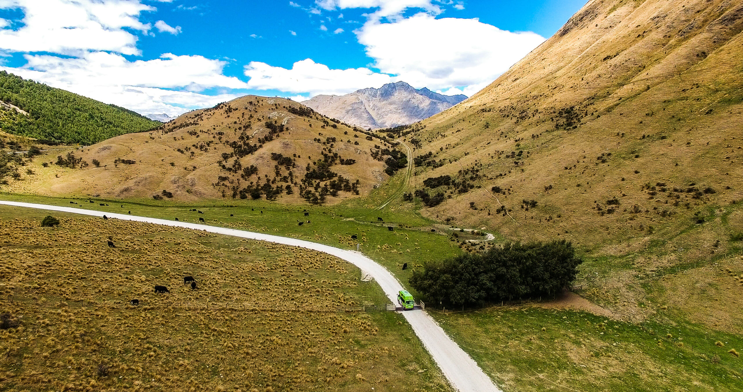 Chaser campervan driving through unpaved NZ road between green hillsides