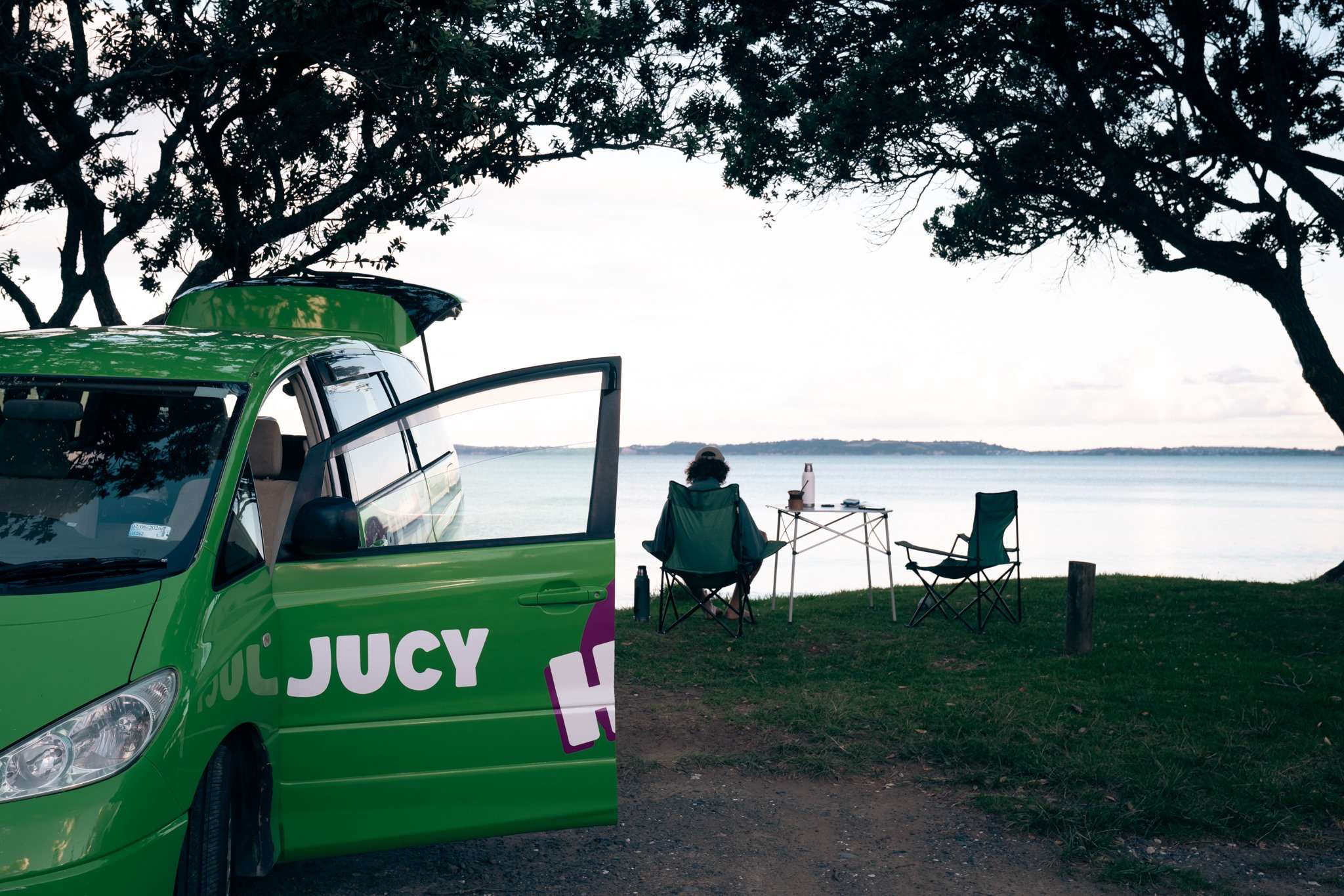 Chilld Cloudbreak parked next to lake with open driver's side door and man sitting at a camping table