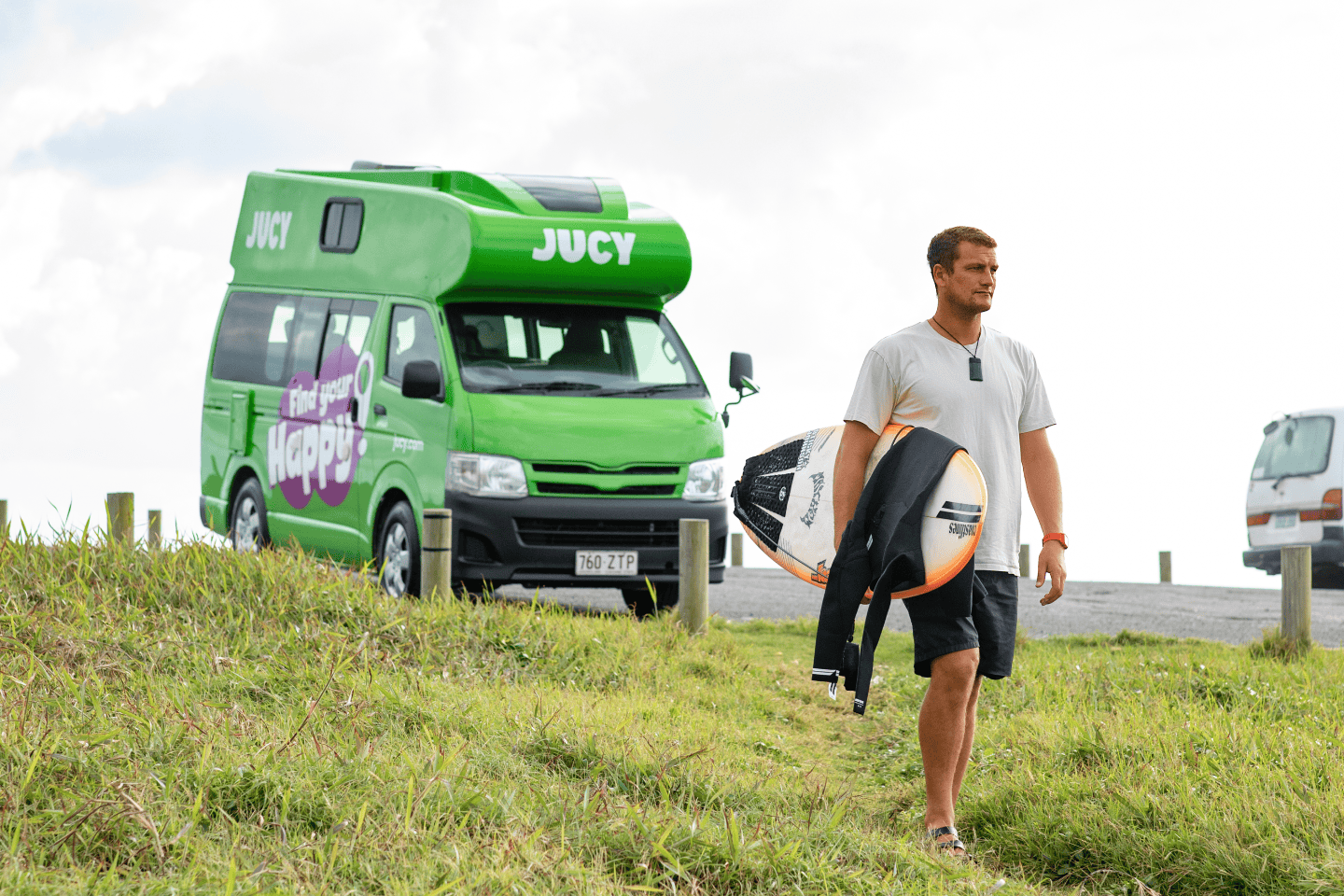 Man carrying surfboard away from parked Condo Campervan