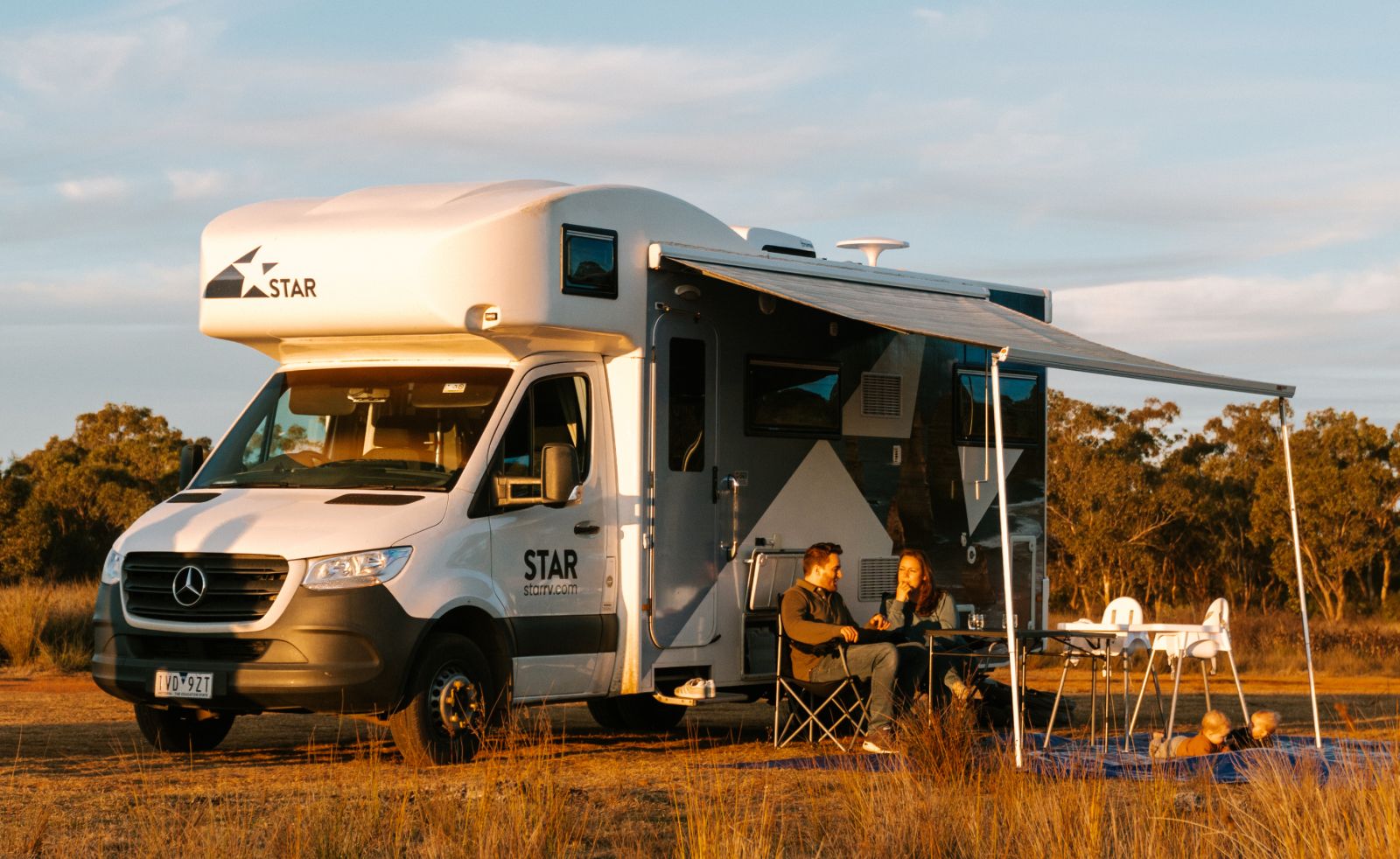 Star RV Polaris 6 parked in field with side awning extended to protect family sitting under it